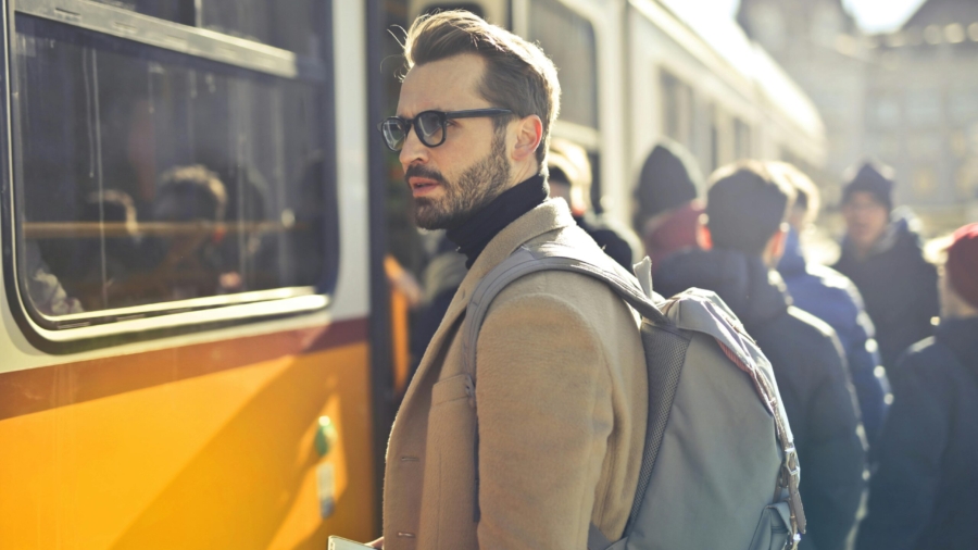 A stylish man with a backpack boards a tram in bustling Budapest, Hungary, during the day.
